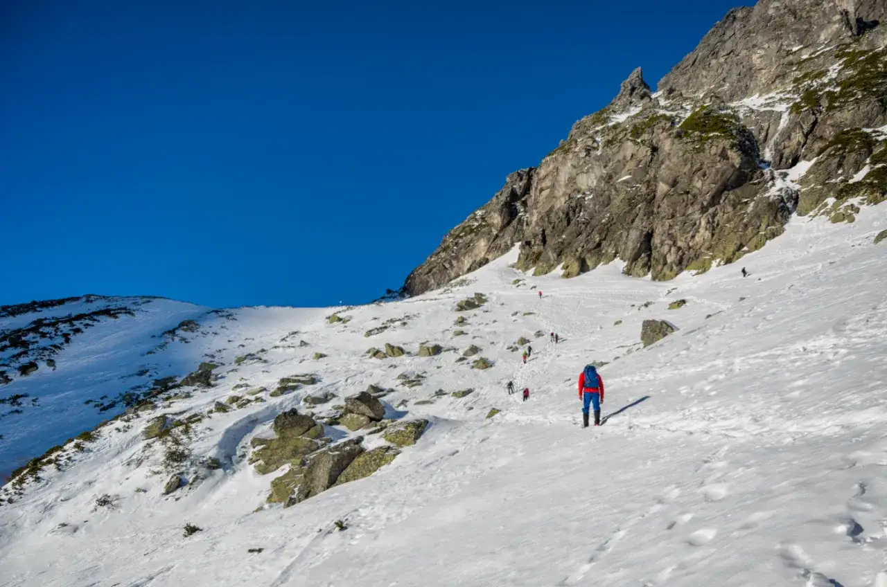 Słoneczny dzień w Tatrach, szlak pokryty śniegiem. Turyści wędrują po zboczu, sprawdzając jakie warunki na szlakach w Tatrach.