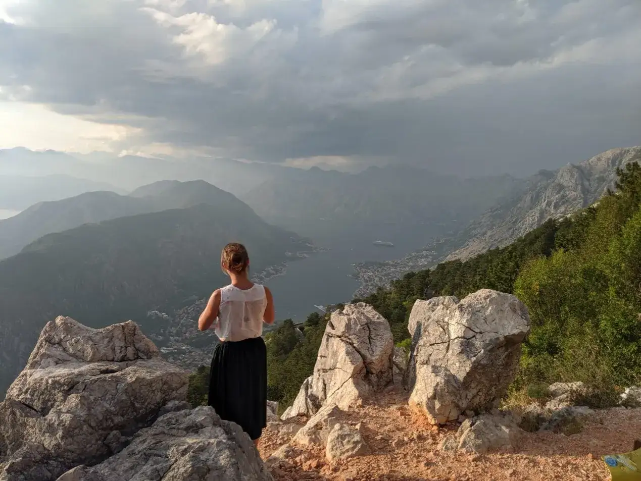 Kobieta podziwia majestatyczne czarnog&oacute;ra g&oacute;ry nad Zatoką Kotorską. Chmury tworzą dramatyczne tło dla krajobrazu.