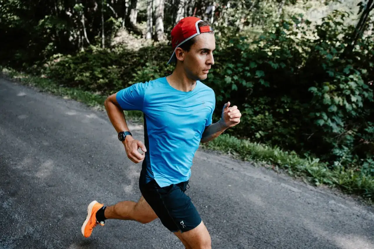 Mężczyzna w niebieskiej koszulce i czerwonej czapce biegnie leśną drogą. Zastanawiasz się, ile kilometrów trzeba przebiec, żeby spalić 1 kg?