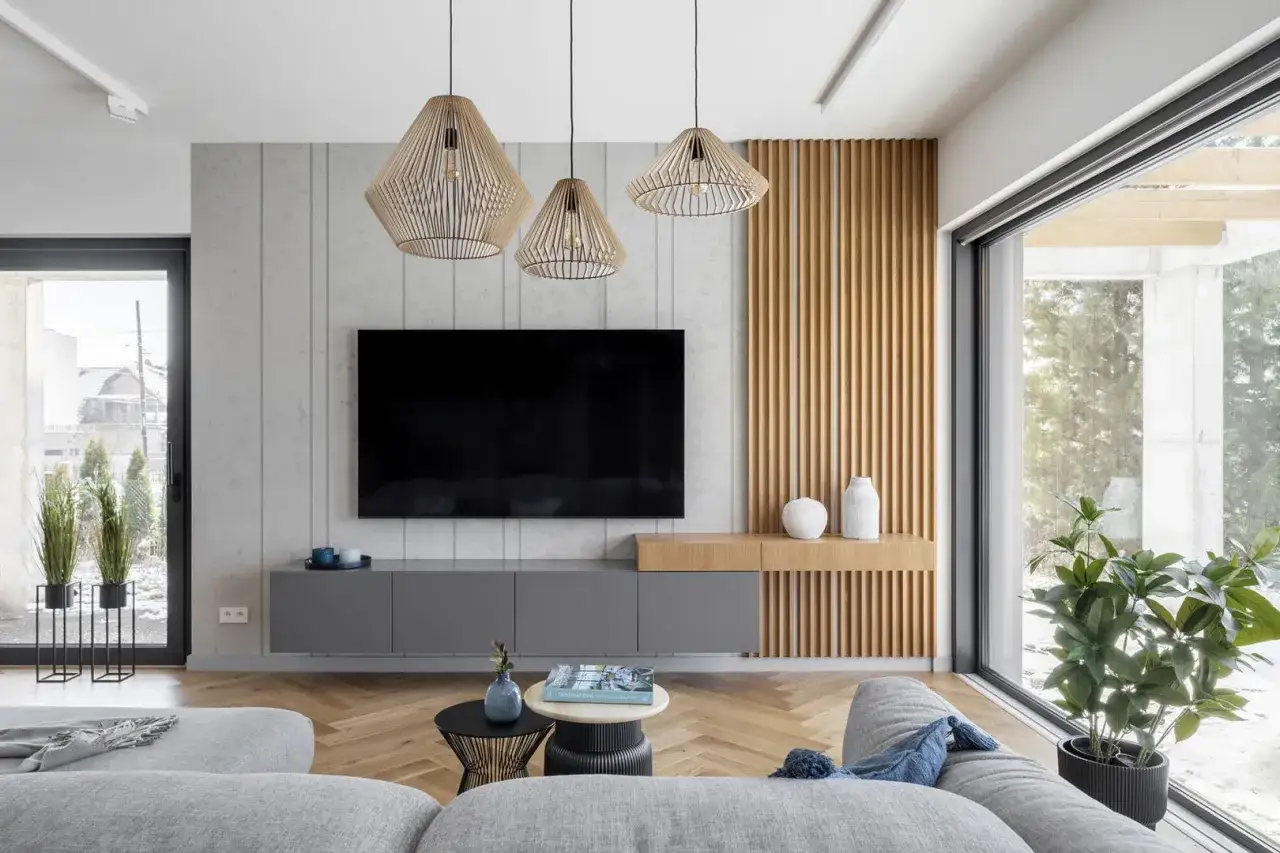 Nowoczesny salon z szarym narożnikiem, drewnianymi panelami i wiszącymi lampami. Aranżacje salonu zachwycają minimalizmem.