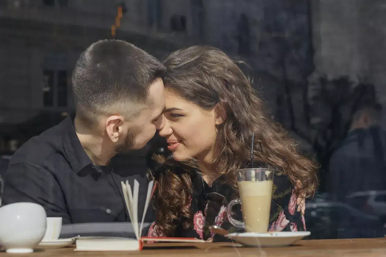 Para zbliża się do siebie podczas randki z Tindera w kawiarni. Na stole kawa i książka.