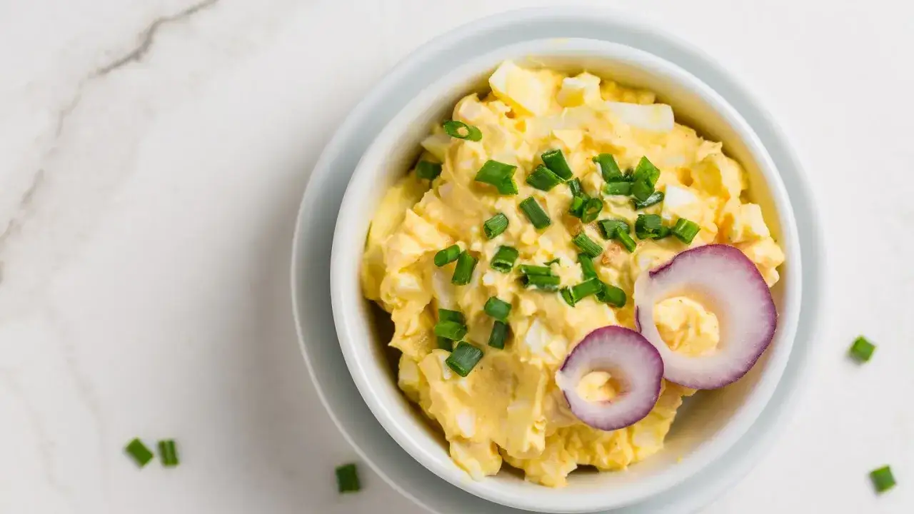 Jak zrobić pastę jajeczną: kremowa masa z jajek, szczypiorku i cebuli, ozdobiona plasterkami czerwonej cebuli.