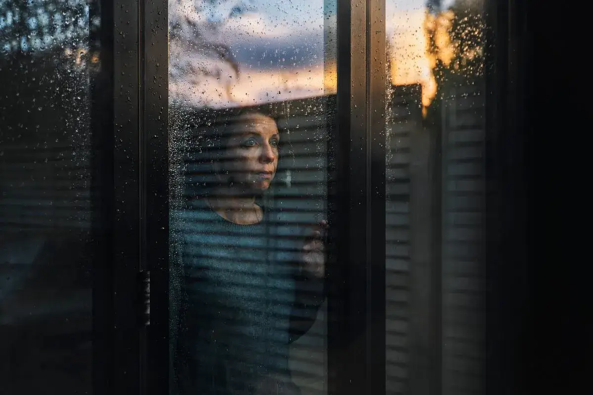 Kobieta patrzy przez zaparowane okno, zastanawiając się, jak zakończyć długoletni związek. Zachodzące słońce maluje niebo na pomarańczowo.