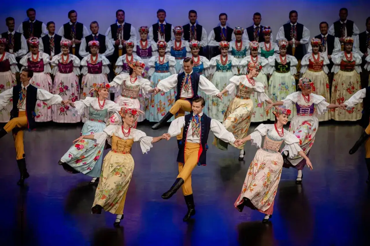 Szła dzieweczka po śląsku, w barwnych strojach ludowych, tańczy z innymi na scenie.