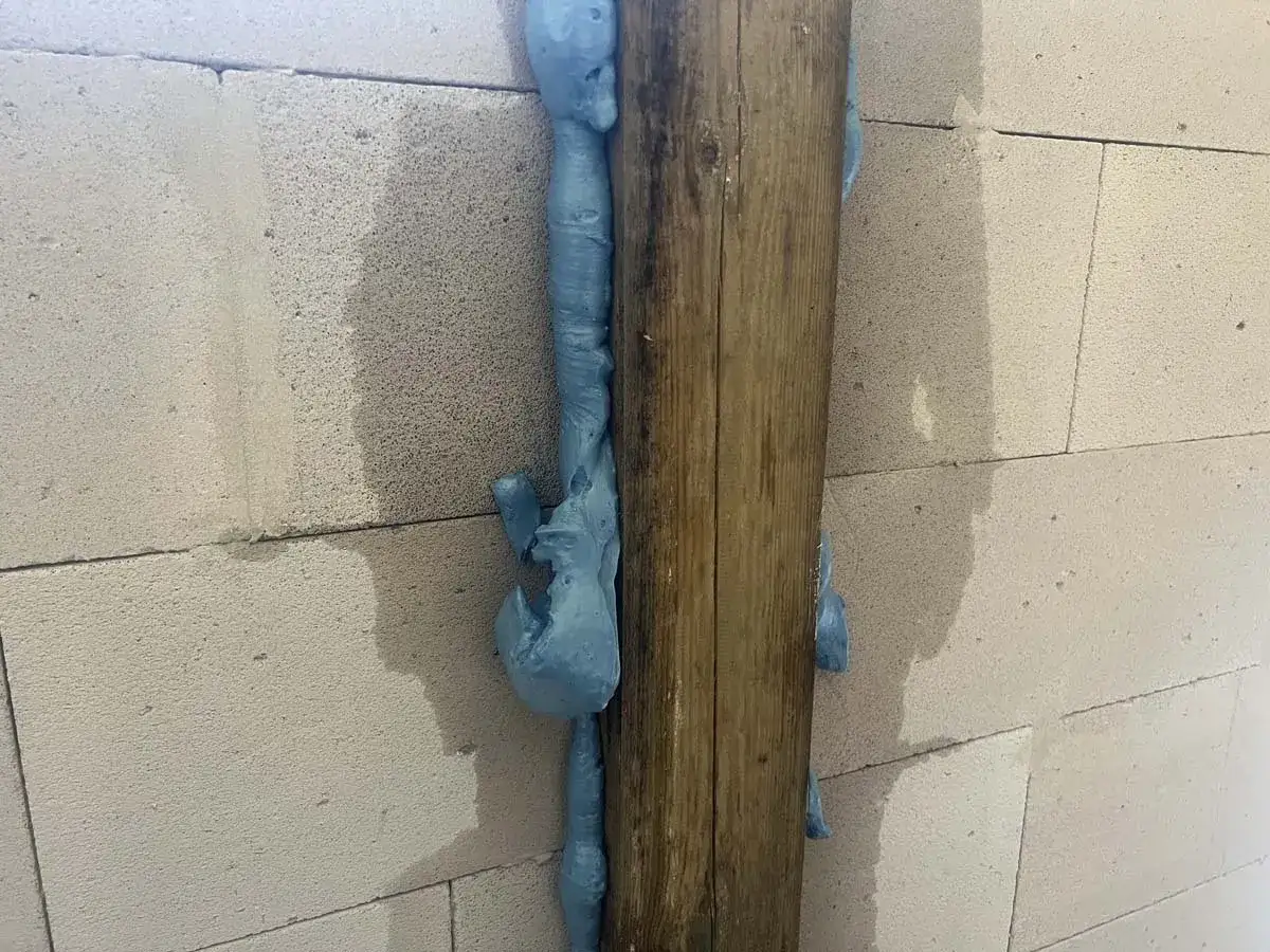 Piana montażowa wypełnia szczelinę między drewnianym słupem a betonowymi bloczkami, pokazując, co to jest dylatacja.