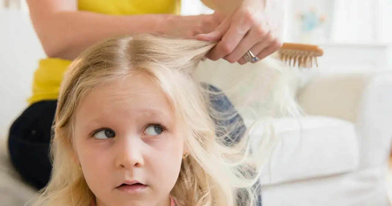Dziecko z blond włosami, które mama czesze. Włosy są jasne, prawie siwe u dziecka, co dodaje im uroku.
