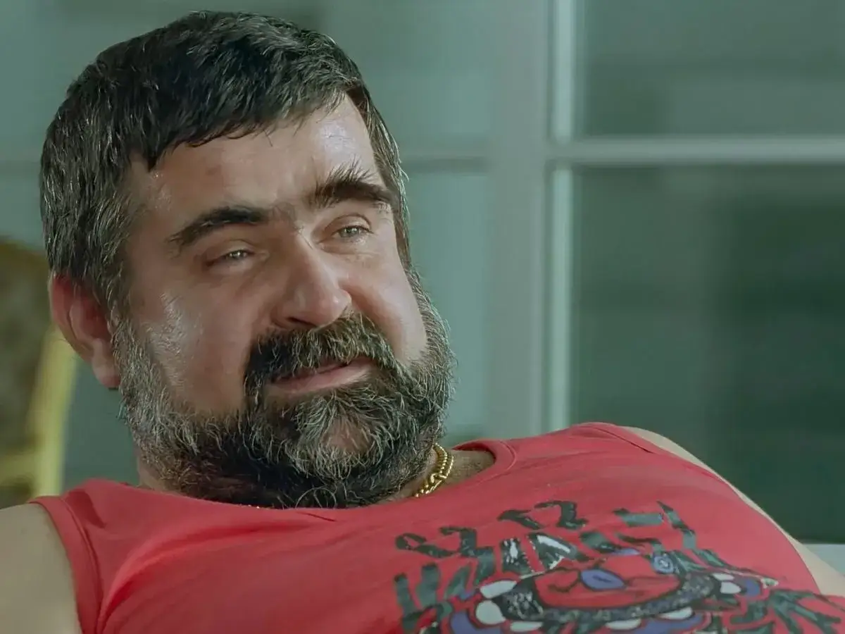 Twarz gangstera z filmu Kiler, z charakterystyczną brodą i w czerwonej koszulce.
