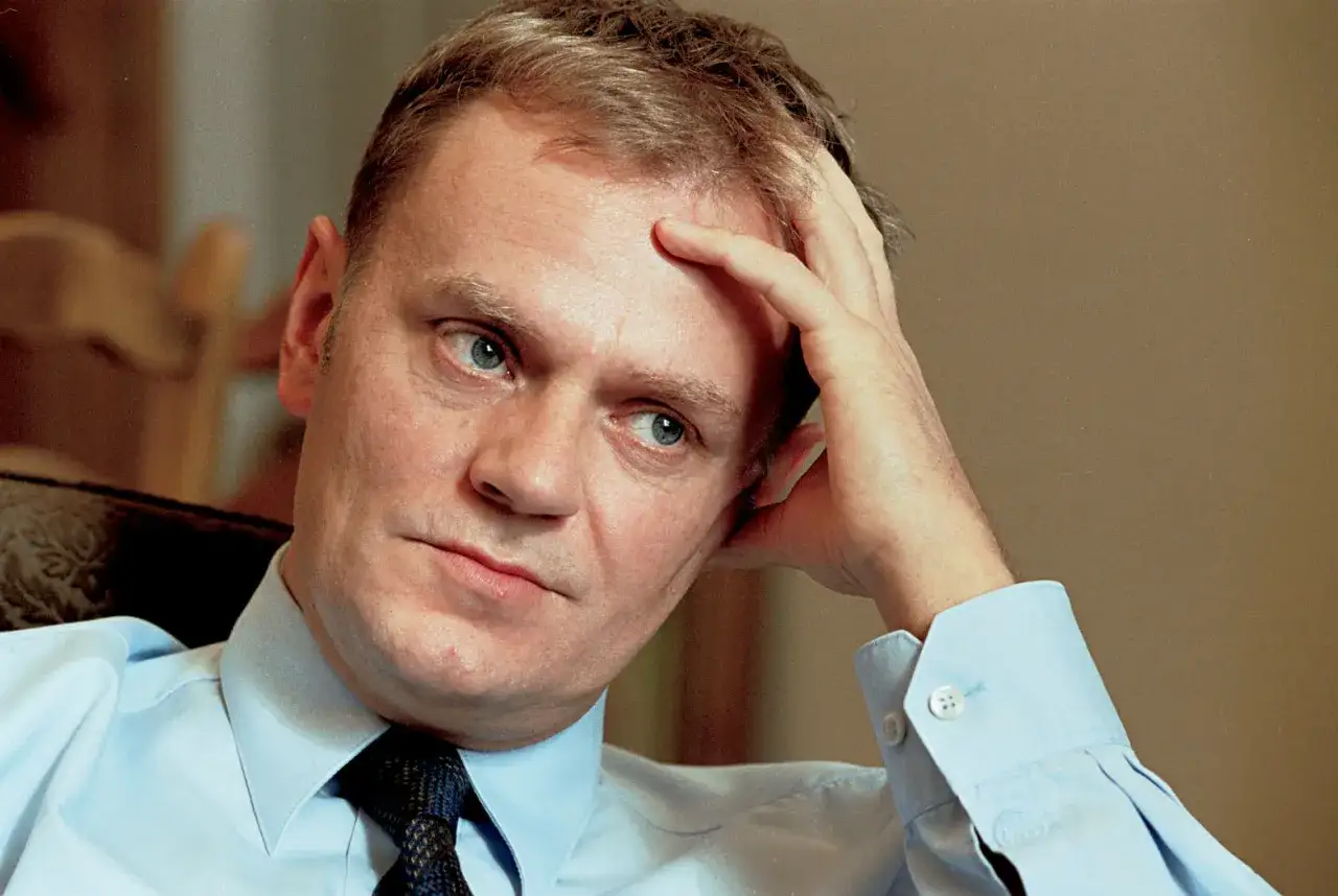 Zamyślony Donald Tusk, zastanawiający się, czy tusk to lewica czy prawica. Jego spojrzenie jest przenikliwe, a dłoń opiera się o czoło.