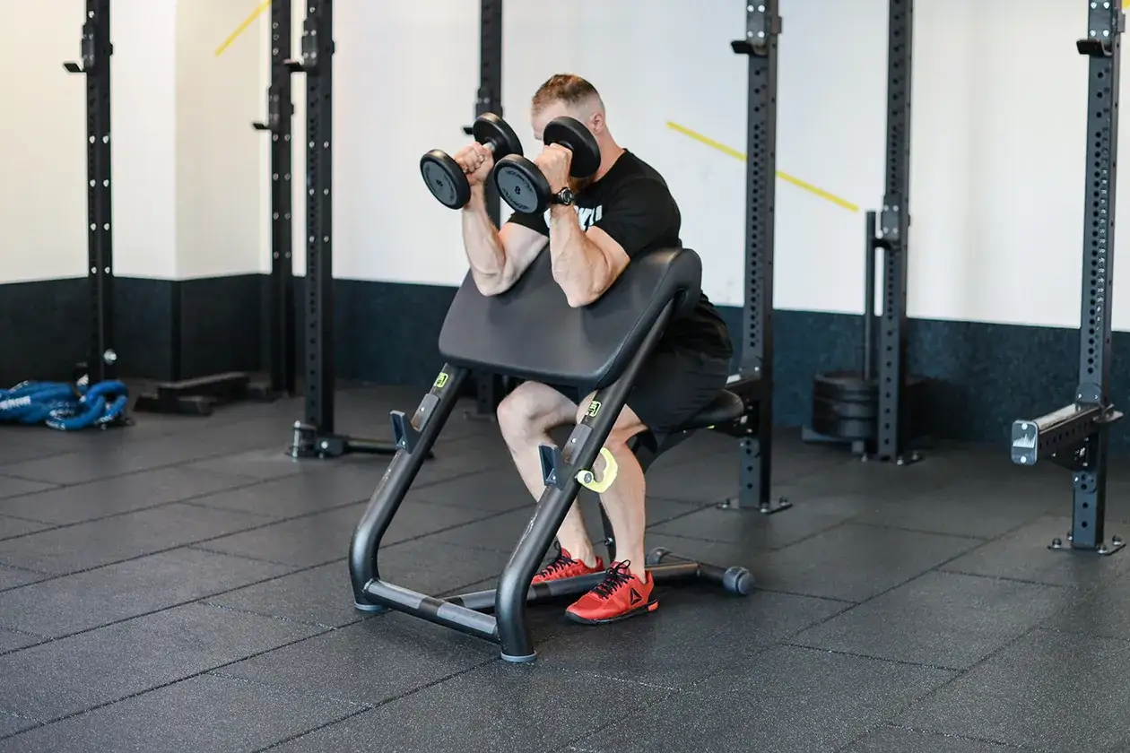 Mężczyzna wykonuje ćwiczenia hammer curls na ławce treningowej, budując siłę bicepsów.