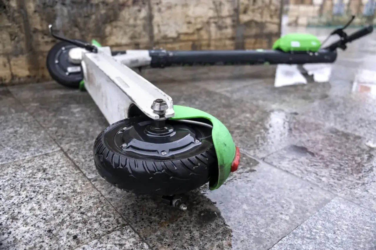 Zostawiony na deszczu rower elektryczny leży na mokrym chodniku.