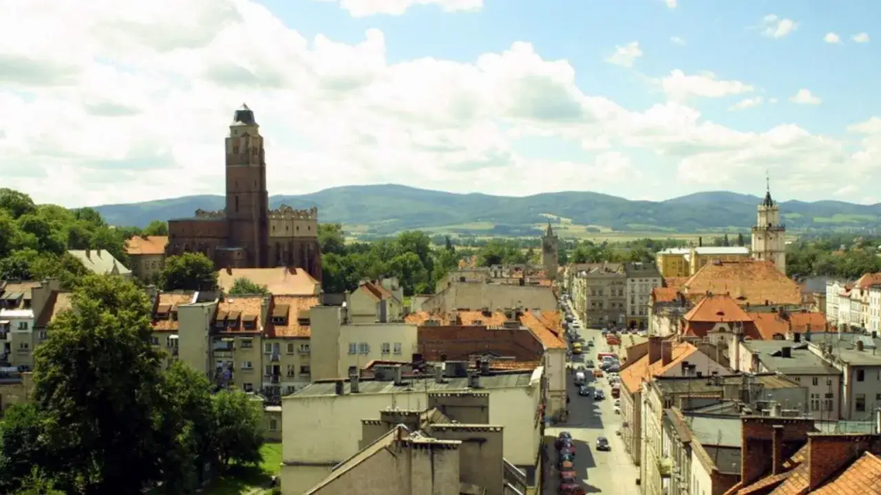 Widok na miasto z g&oacute;rami w tle. Widać wieżę kościelną i ratusz, kt&oacute;re są gł&oacute;wnymi paczk&oacute;w atrakcje.