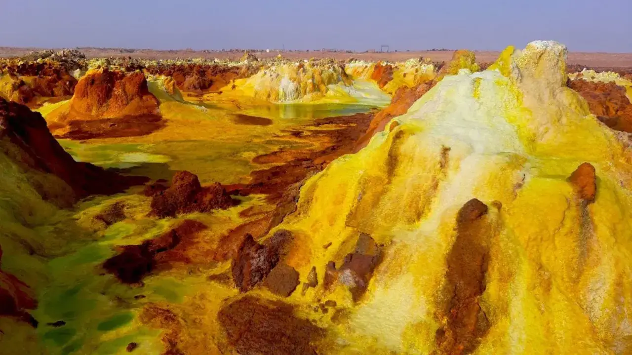 Krajobraz jak z innej planety w Kotlinie Danakilskiej. Ż&oacute;łte i pomarańczowe formacje skalne otaczają zielonkawe jeziorka.