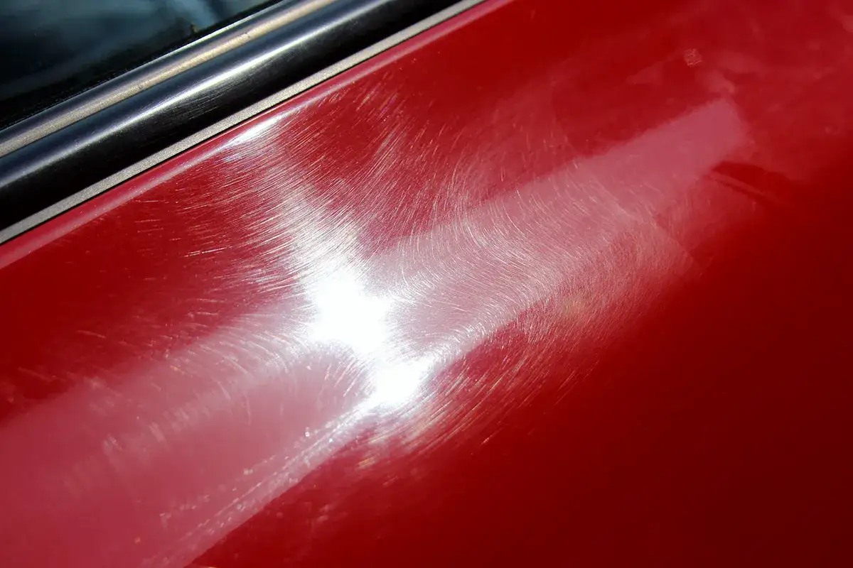 Widoczne rysy na czerwonym lakierze samochodu. Czy myjnia automatyczna niszczy lakier? Te ślady sugerują, że tak.