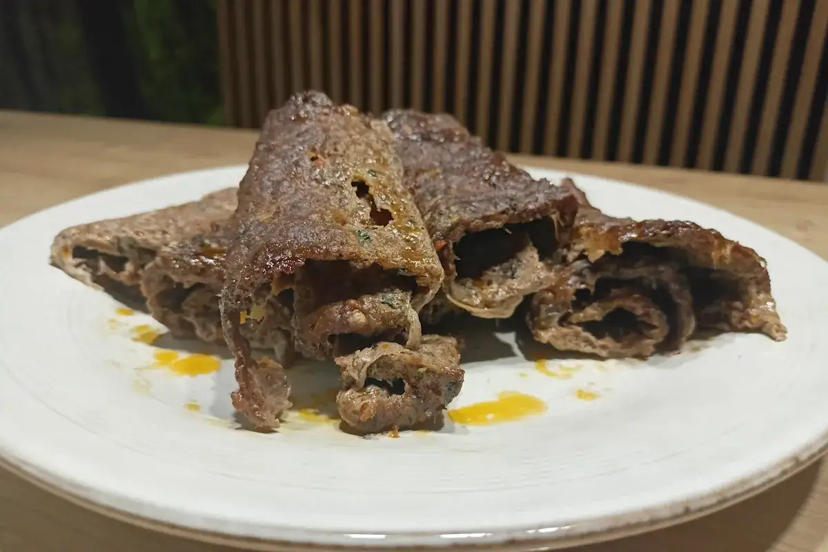 Soczysty kebab w piekarniku, zawinięty w cienkie plastry mięsa, podany na talerzu z żółtym sosem.