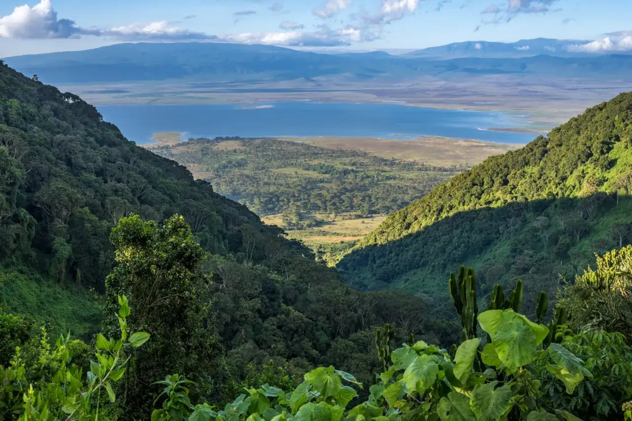 Widok z góry na zielone zbocza i jezioro w Ngorongoro Crater. Słońce oświetla część krajobrazu.