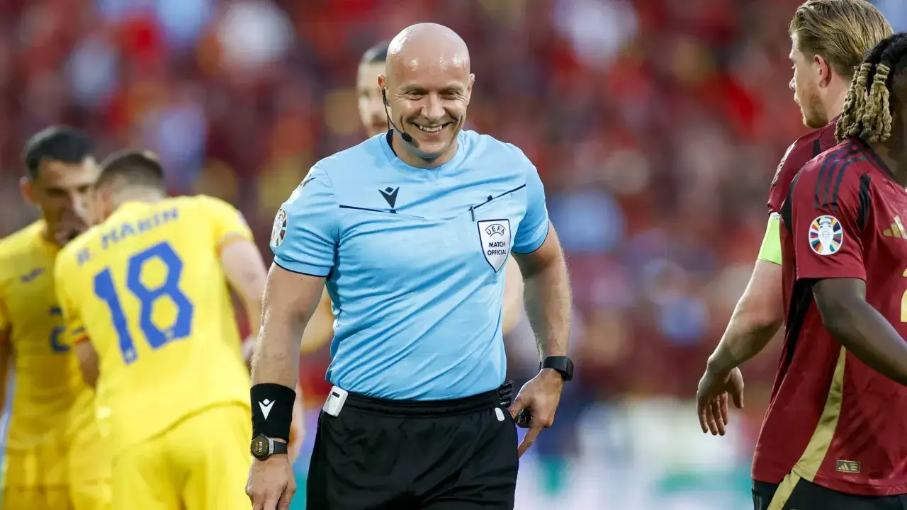 Uśmiechnięty sędzia piłkarski w Lidze Mistrzów, w tle zawodnicy. Ciekawe, ile zarabia sędzia piłkarski w lidze mistrzów za takie emocje.