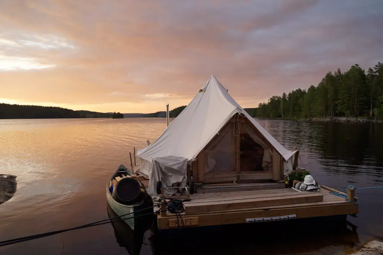 Pływający namiot na tratwie, gotowy na nocleg nad jeziorem o zachodzie słońca.