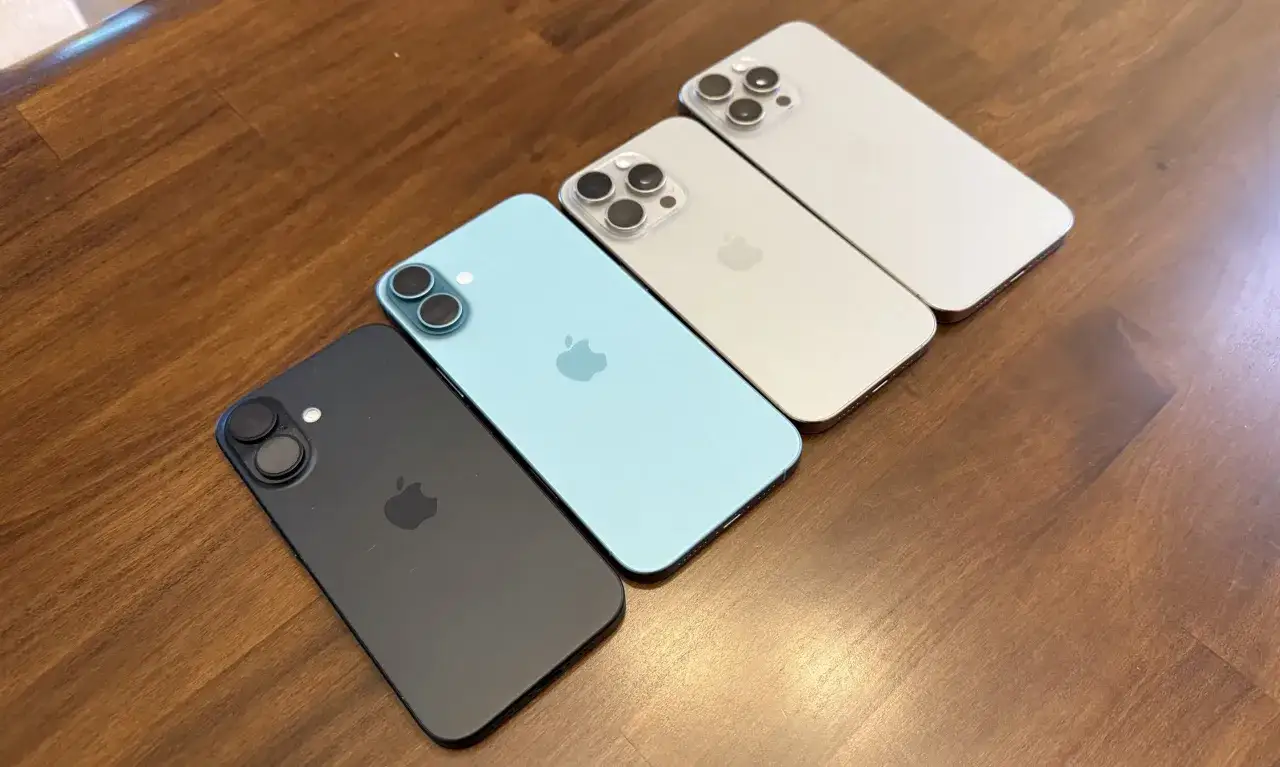 Cztery iPhone'y ułożone na drewnianym blacie. Dwa modele z trzema aparatami, jeden z dwoma, a najmniejszy iPhone z 4 aparatami z tyłu.