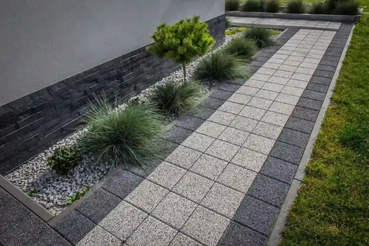 Nowoczesna opaska wok&oacute;ł domu z kostki brukowej i zieleni.