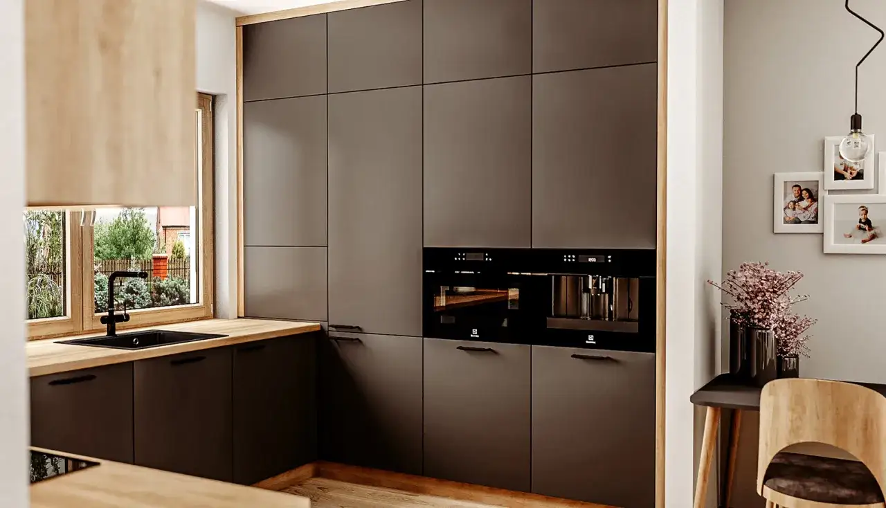 Nowoczesna kuchnia z ciemnymi frontami i drewnianym blatem. Okno w kuchni znajduje się na wygodnej wysokości, nad zlewem.