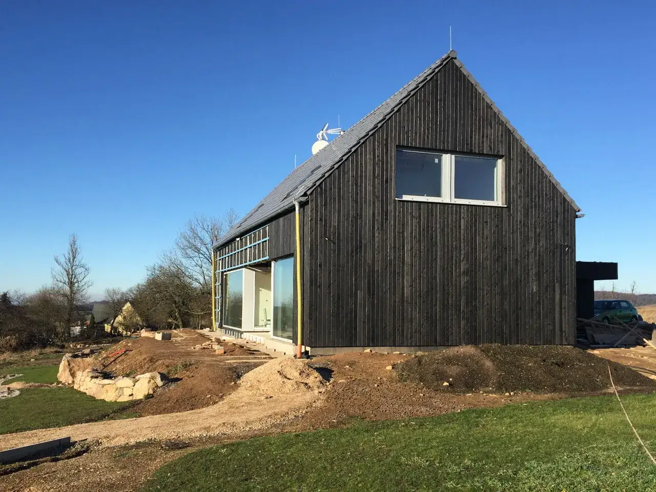 Nowoczesny dom z opalanej deski, idealny do ochrony czym pomalować opalane drewno. Teren wok&oacute;ł w budowie.