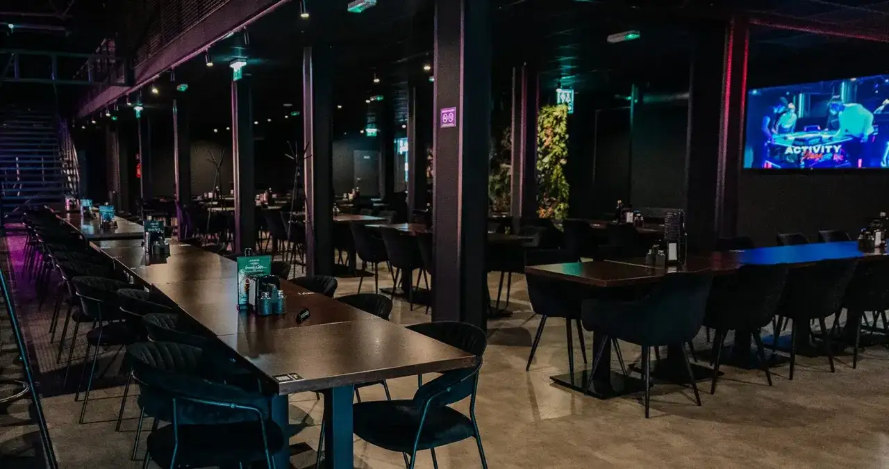 Nowoczesne wnętrze z długimi stołami i czarnymi krzesłami. Idealne miejsce na imprezę dla 40 osób.