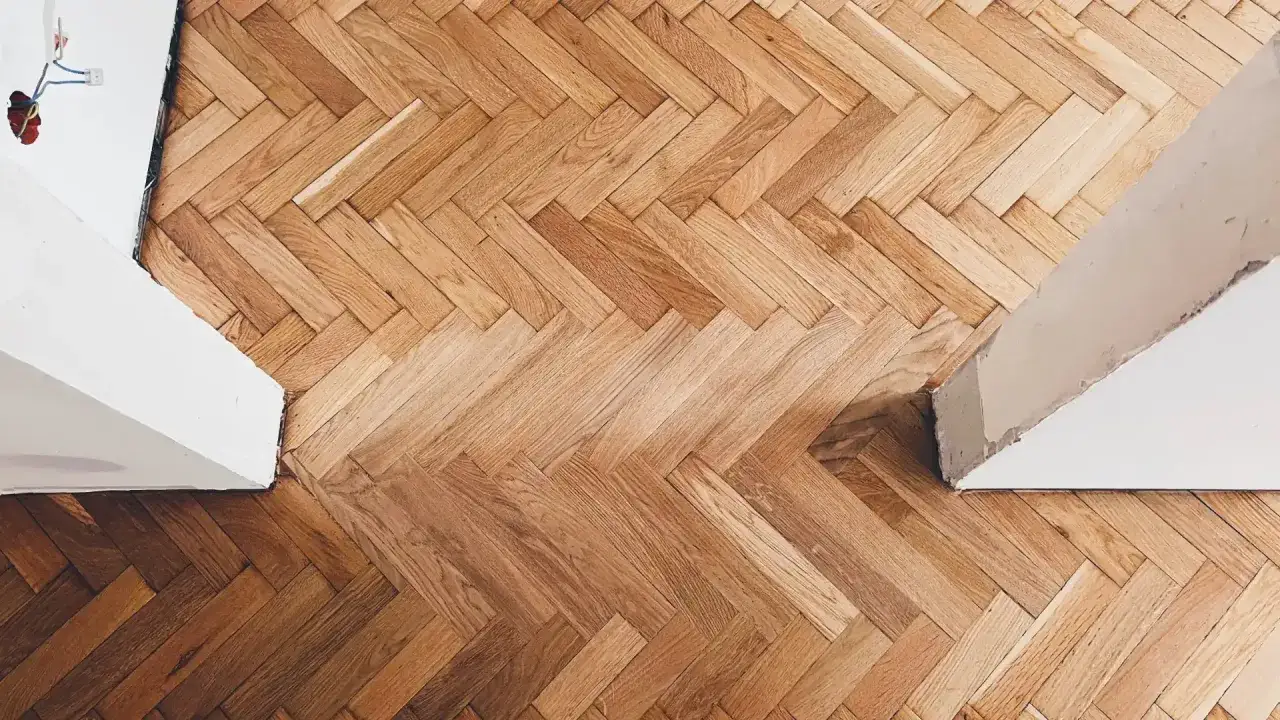 Drewniany parkiet ułożony we wzór jodełki, gotowy do malowania parkietu bez cyklinowania. Widać białe ściany i fragmenty instalacji elektrycznej.