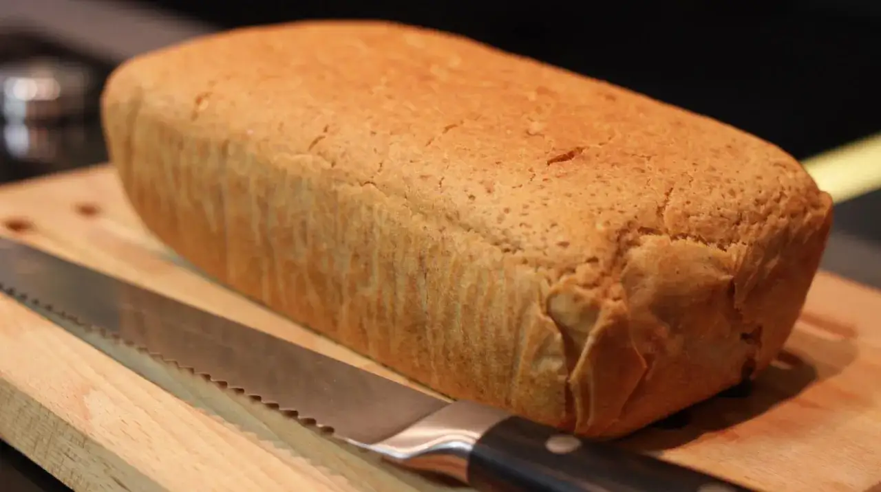 Chleb tostowy bezglutenowy przepis: złocisty bochenek na desce z nożem. Idealny do przygotowania pysznych kanapek.