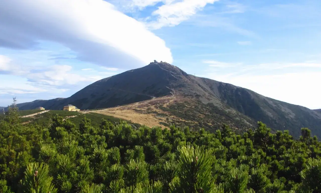Widok na najwyższe szczyty Karkonoszy, Śnieżkę, z budynkami na szczycie i szlakiem turystycznym.