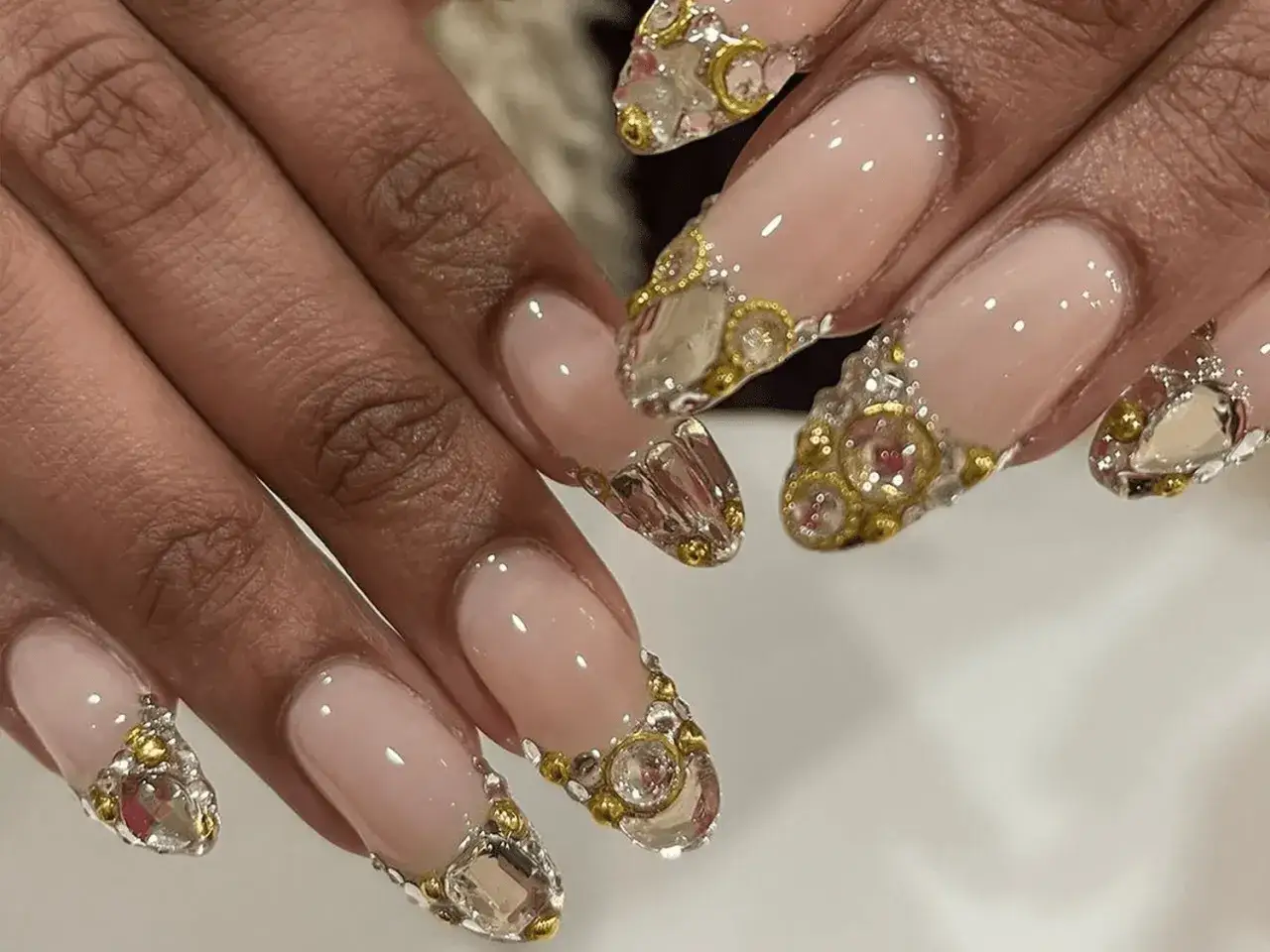 Eleganckie paznokcie french z diamencikami, zdobione złotymi koralikami i kryształkami, wyglądają jak biżuteria.