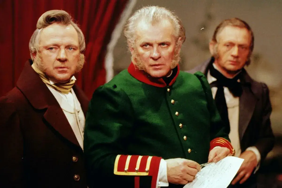 Tadeusz Łomnicki w zielonym mundurze, w otoczeniu aktor&oacute;w, przypomina scenę z film&oacute;w i seriali.