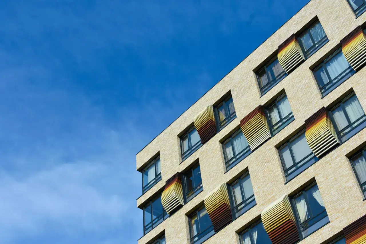 Nowoczesny budynek z cegły, z oknami i kolorowymi żaluzjami. Każdy lokal stanowiący odrębną nieruchomość ma swój unikalny charakter.