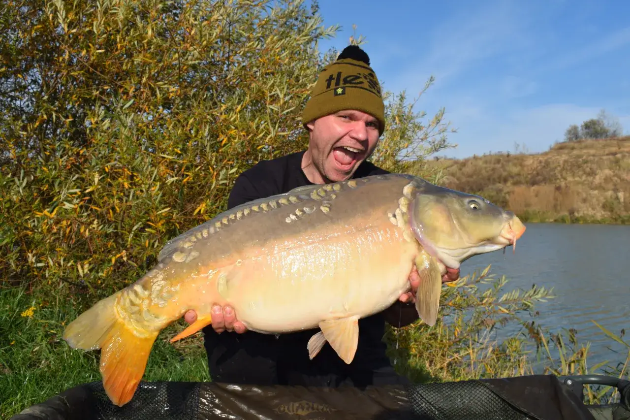 Szczęśliwy wędkarz z okazałym karpiem na tle zielonej wyspy. Wspaniały połów na łowisku!