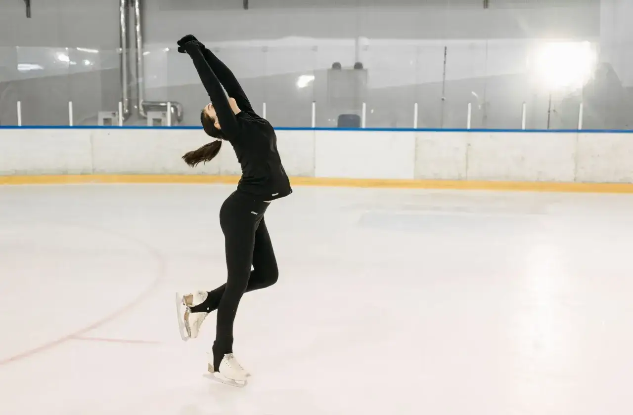 Młoda kobieta w czarnym stroju wykonuje piruet podczas treningu jazdy figurowej na lodzie.