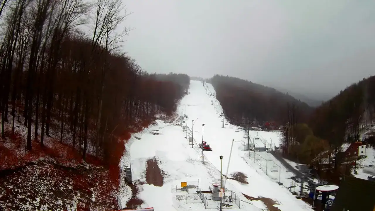 Widok z kamery na stok narciarski w Gołębiewski Wisła. Śnieg, wyciągi krzesełkowe i ratrak przygotowują trasę.