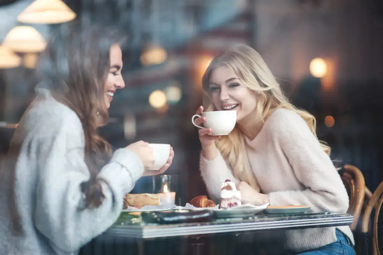 Dwie przyjaci&oacute;łki śmieją się przy kawie i ciastku. Dzielą się sekretami i zadają sobie pytania do przyjaci&oacute;łki.