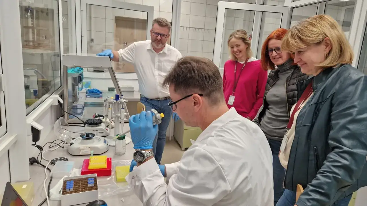 Naukowcy w laboratorium analizują próbki. Dyskusja o tym, ile zarabia biolog, trwa w tle.