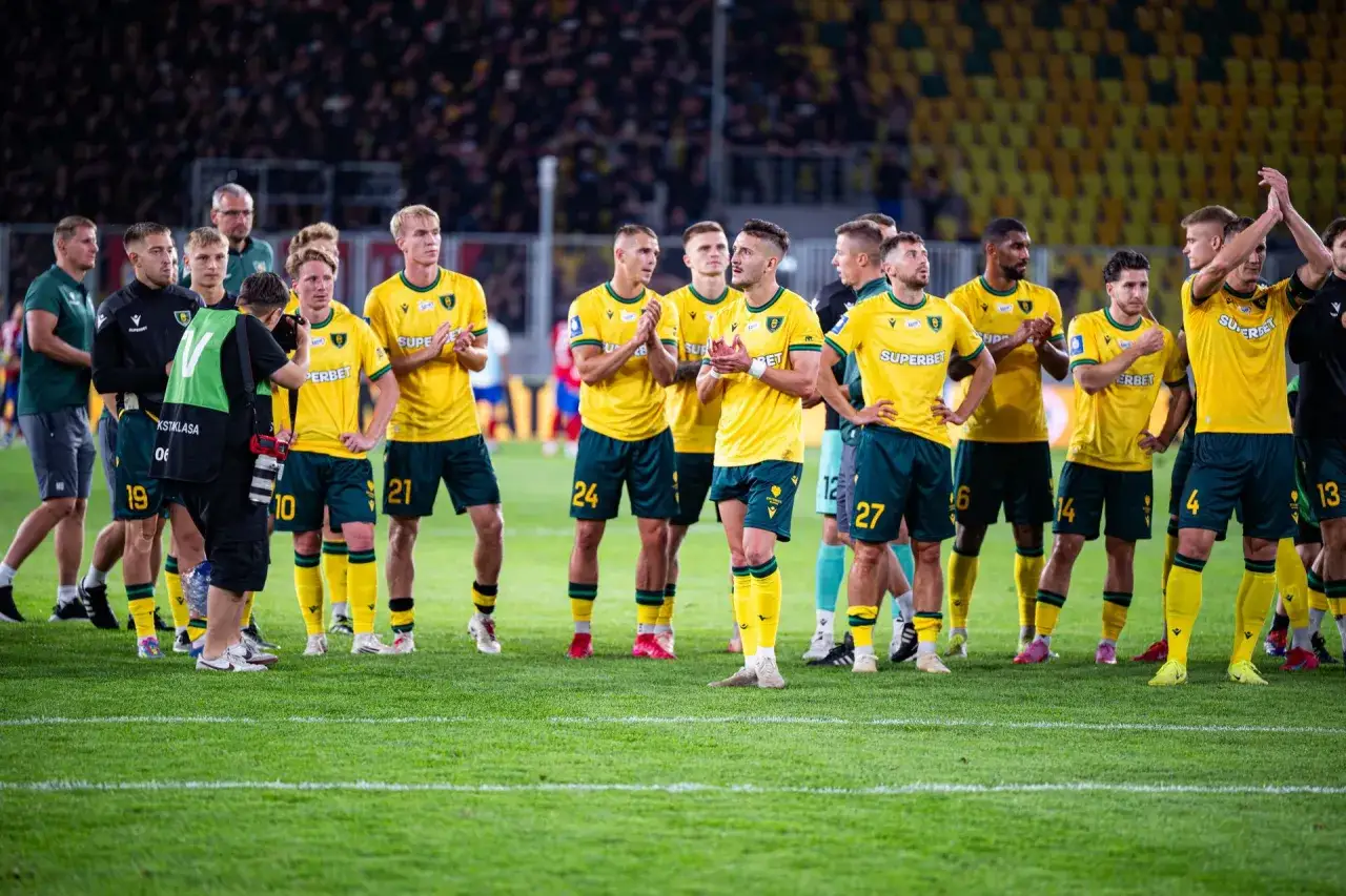 Piłkarze GKS Katowice w żółtych strojach stoją na murawie, pozdrawiając kibiców.