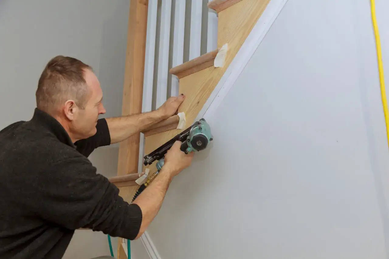 Mężczyzna przybija gwoździami drewniane stopnie schod&oacute;w, pokazując, jak odnowić schody drewniane.