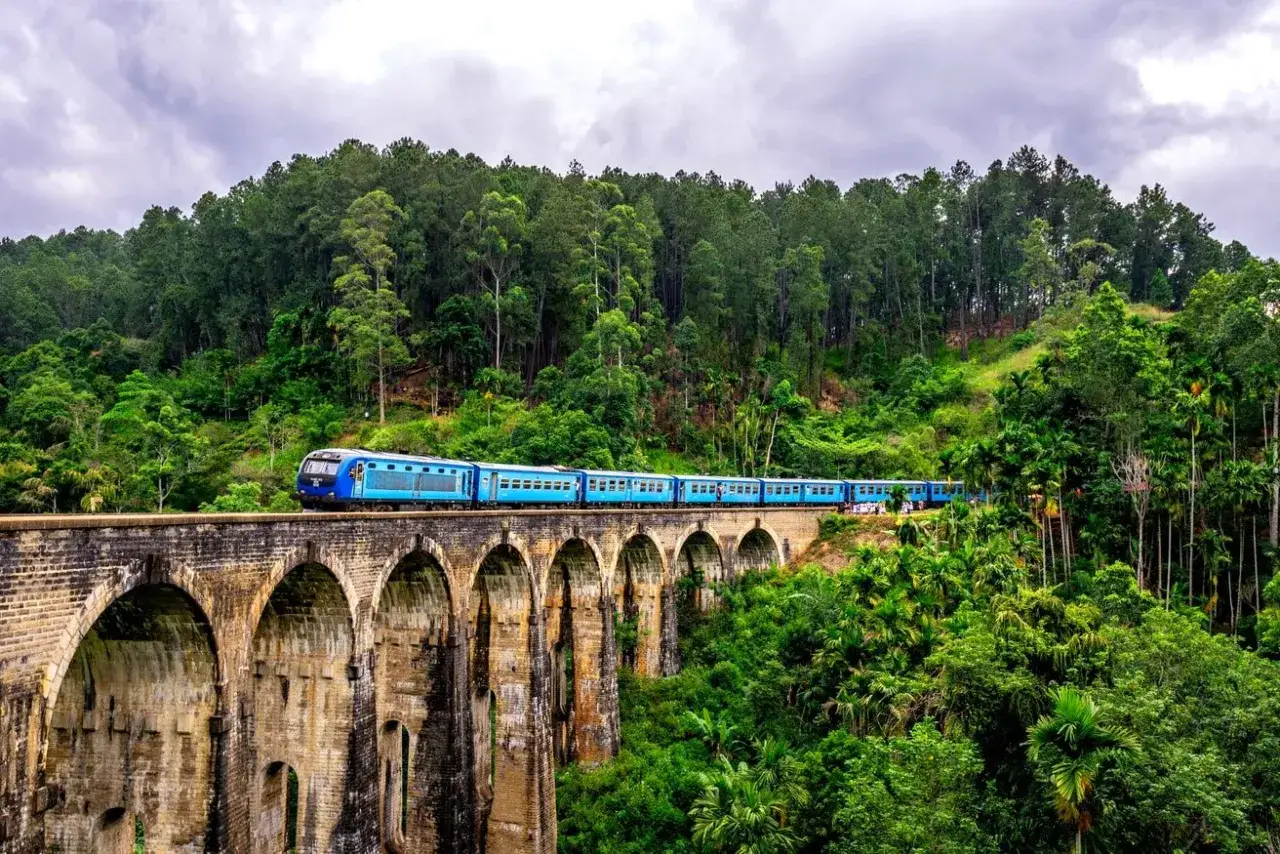 Niebieski pociąg przejeżdża przez dziewięciookowy most w otoczeniu bujnej zieleni. Podróżowanie po Sri Lance jest bezpieczne, a widoki zapierają dech w piersiach.