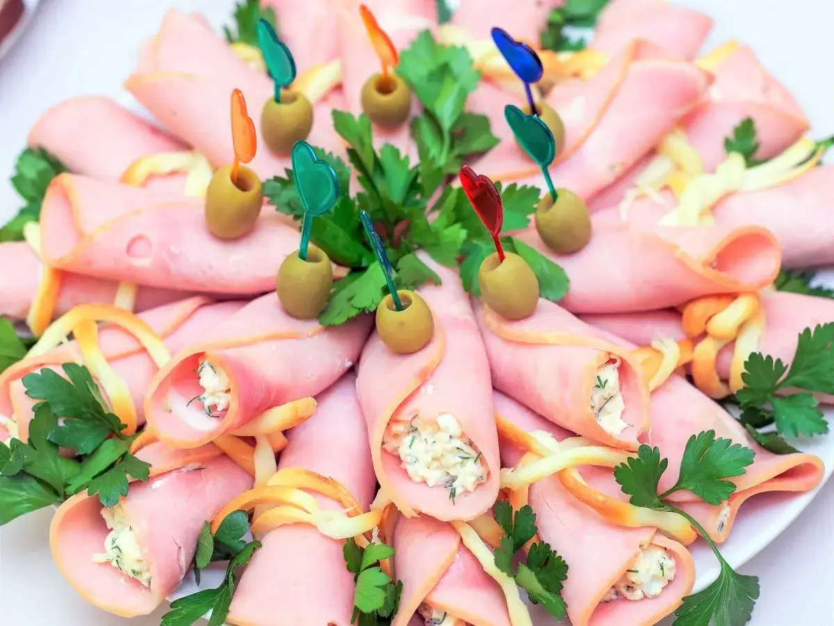 Roladki z szynki z serem i ziołami, ozdobione oliwkami i kolorowymi wykałaczkami. Pyszna przekąska na przyjęcie.