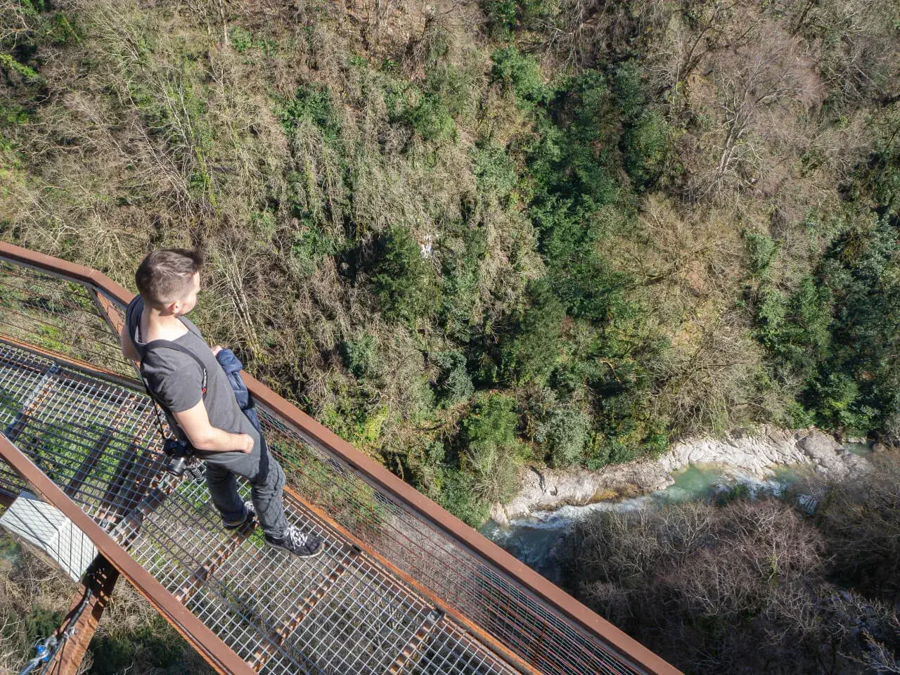 Mężczyzna na metalowej kładce nad wąwozem z rzeką. Widok z góry. Czy w Gruzji jest bezpiecznie? Tak, jeśli zachowasz ostrożność.