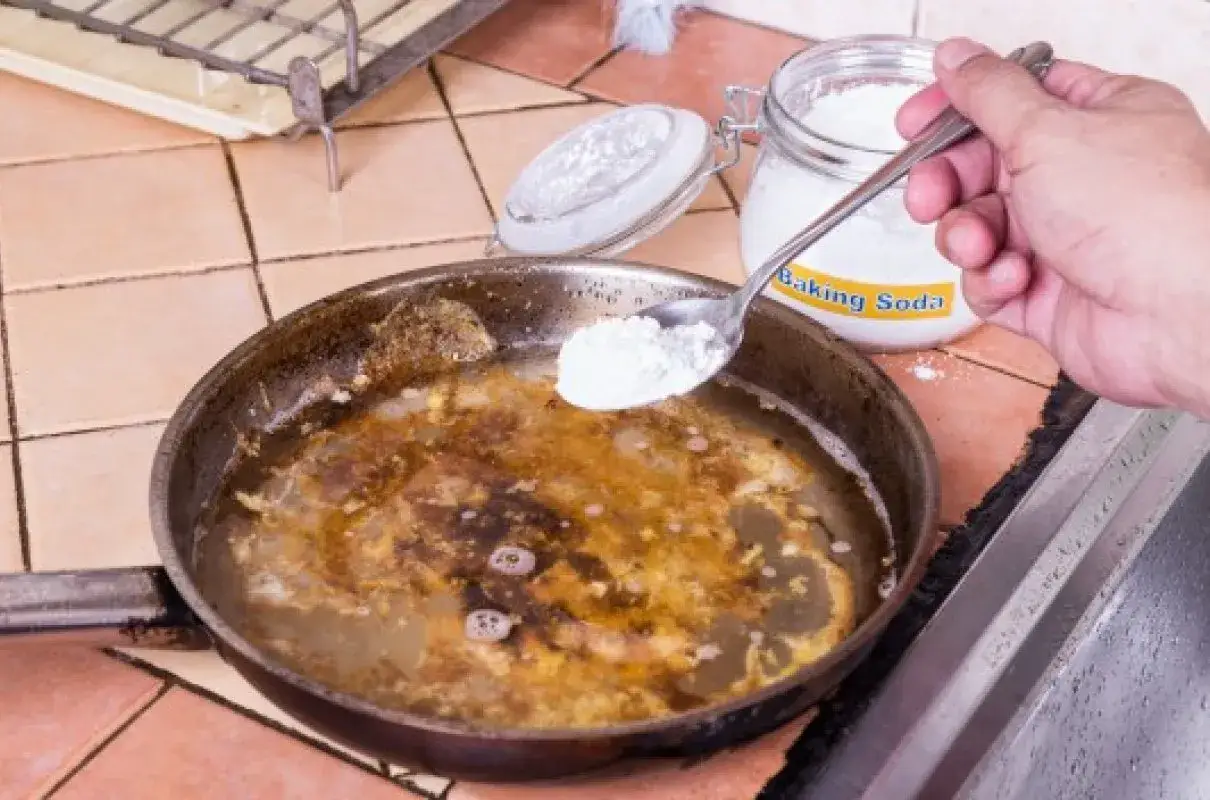 Czyszczenie patelni sodą i octem: dodawanie sody do brudnej patelni z wodą, aby usunąć przypalony tłuszcz.