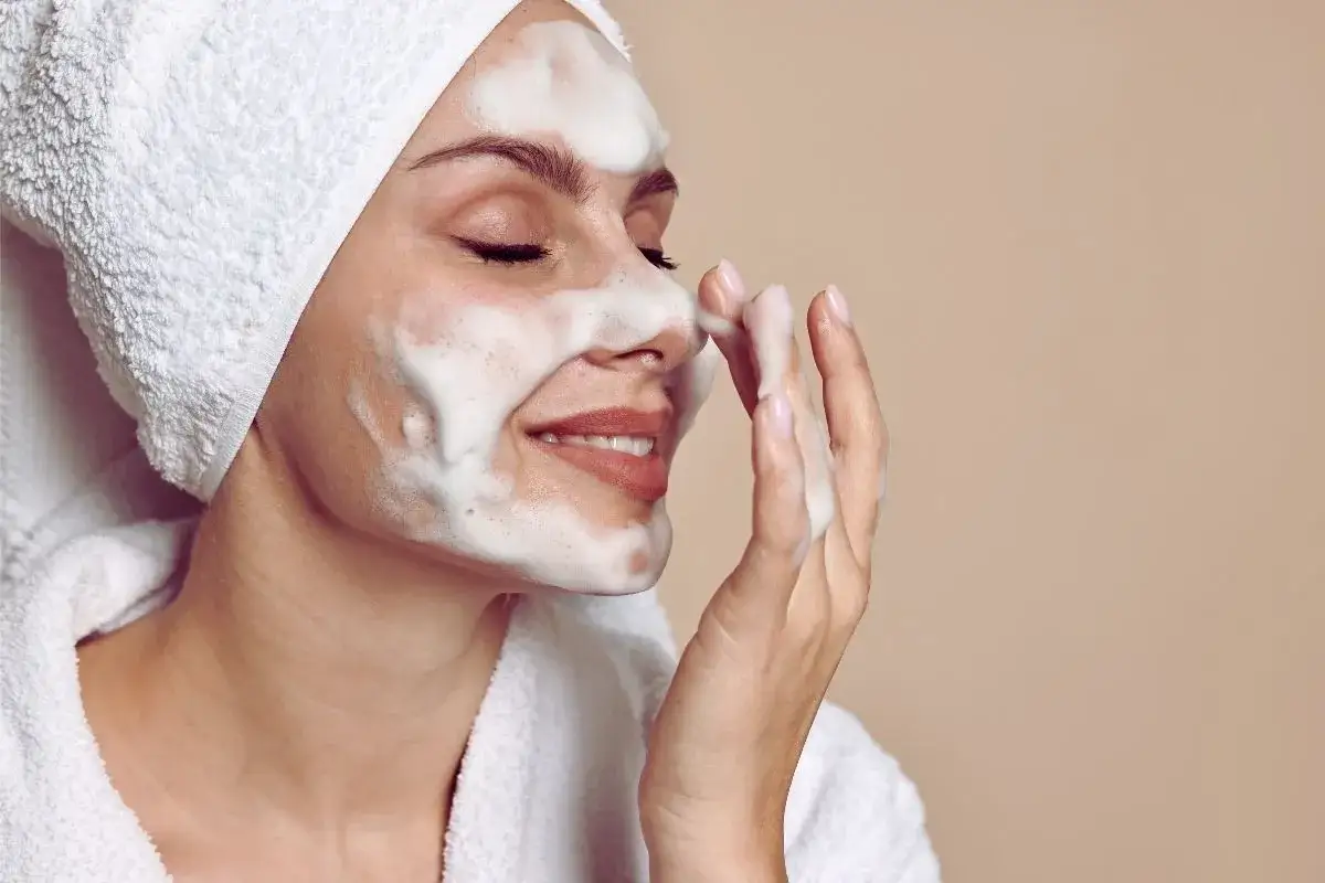Kobieta z pianką na twarzy, w ręczniku na głowie i szlafroku. To idealny moment na dwuetapowe oczyszczanie twarzy dla promiennej cery.