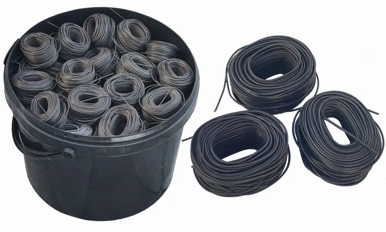 Duży czarny kubeł wypełniony motkami drutu wiązałkowego. Obok trzy luźne zwoje drutu.