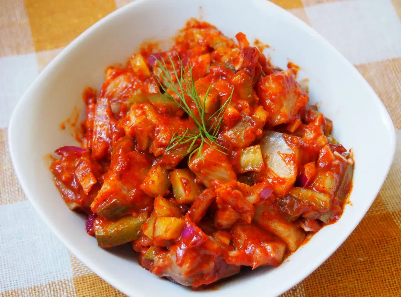 Pyszne śledzie po cygańsku w sosie pomidorowym z dodatkiem cebuli i og&oacute;rka, udekorowane gałązką koperku.