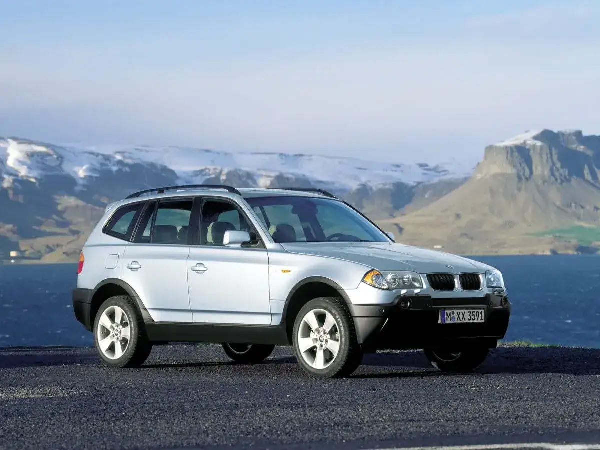 Srebrne BMW X3 E83 na tle malowniczego, zimowego krajobrazu z górami i wodą.