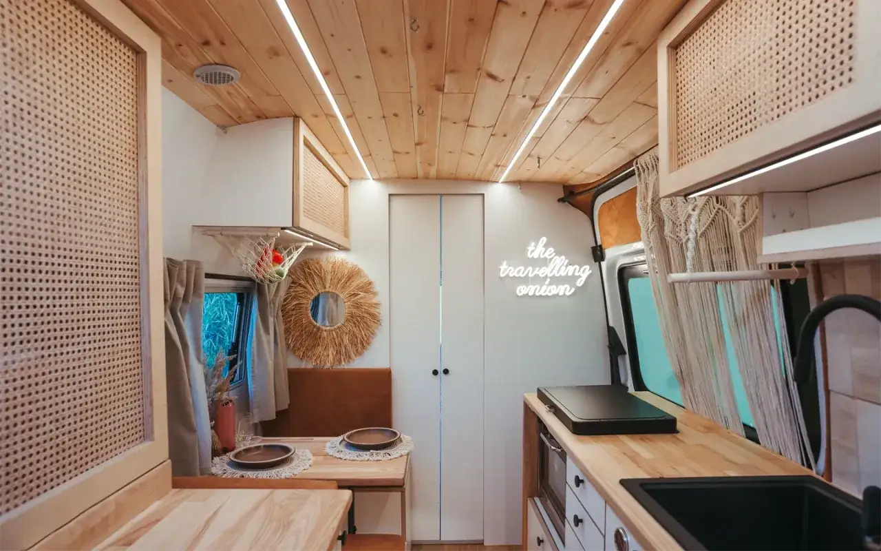 Przytulne wnętrze van camper z drewnianym sufitem, rattanowymi panelami i neonowym napisem 