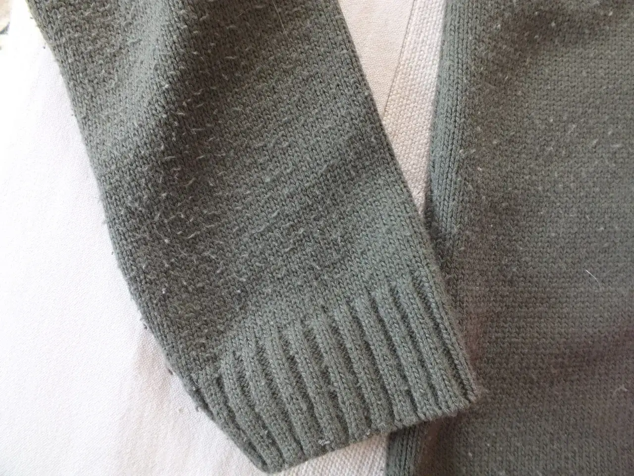 Mechacący się sweter w kolorze khaki. Widać drobne kuleczki na dzianinie, co wyjaśnia, dlaczego swetry się mechacą.