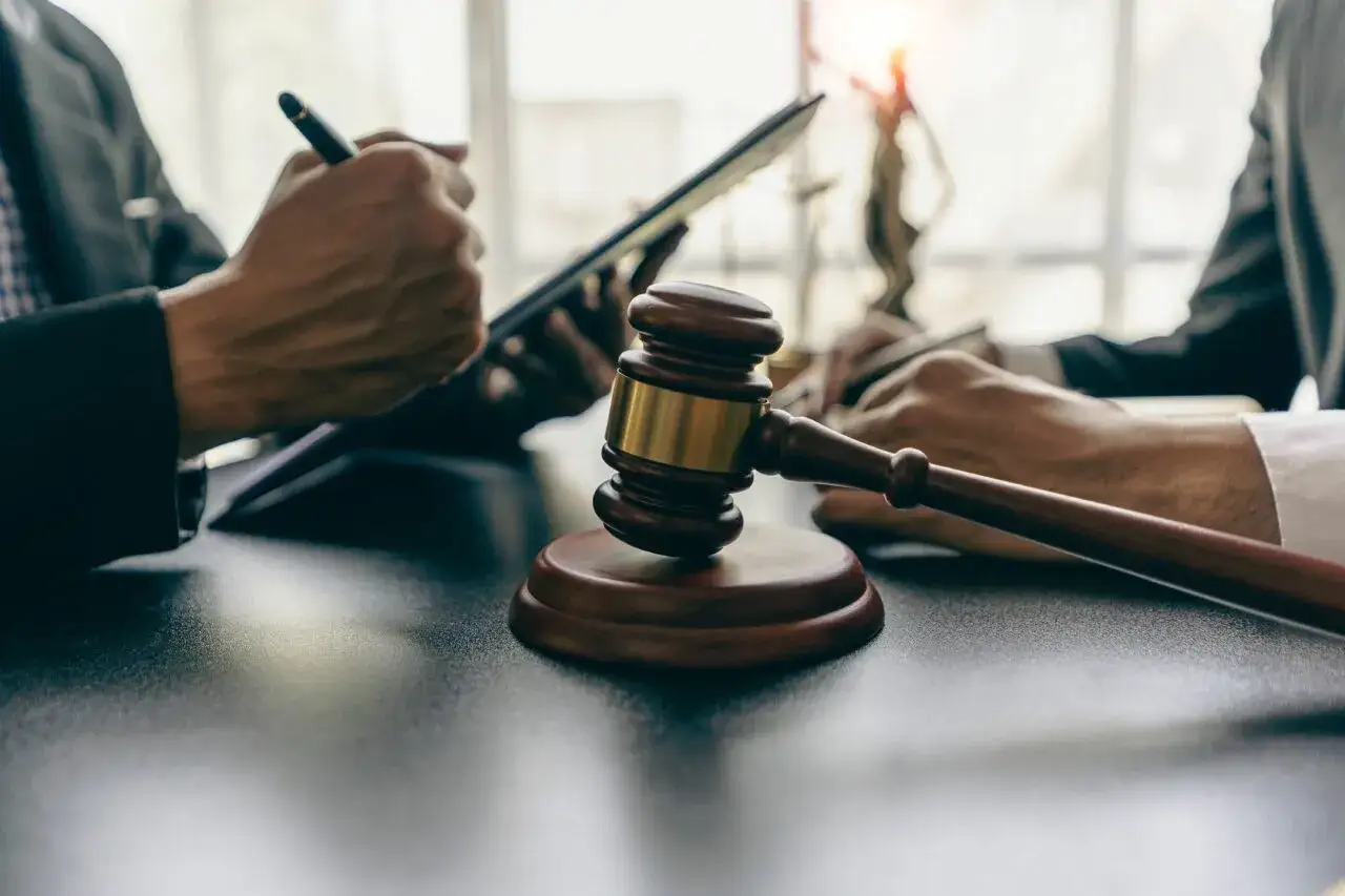 Sądowy młotek i ręce prawników analizujących dokumenty. W tle widoczna Temida. To symbol finalnego orzeczenia, które może opierać się na opinii biegłego.